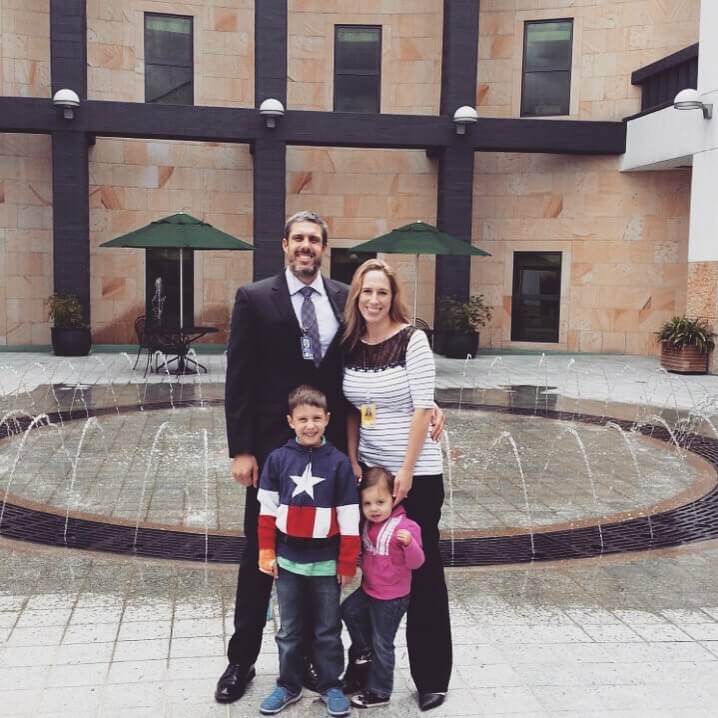 Man and woman stand smiling with two young children in front of a circular fountain in a tiled courtyard with tan stone walls. The photo captures a family moment during everyday life in Cartagena.