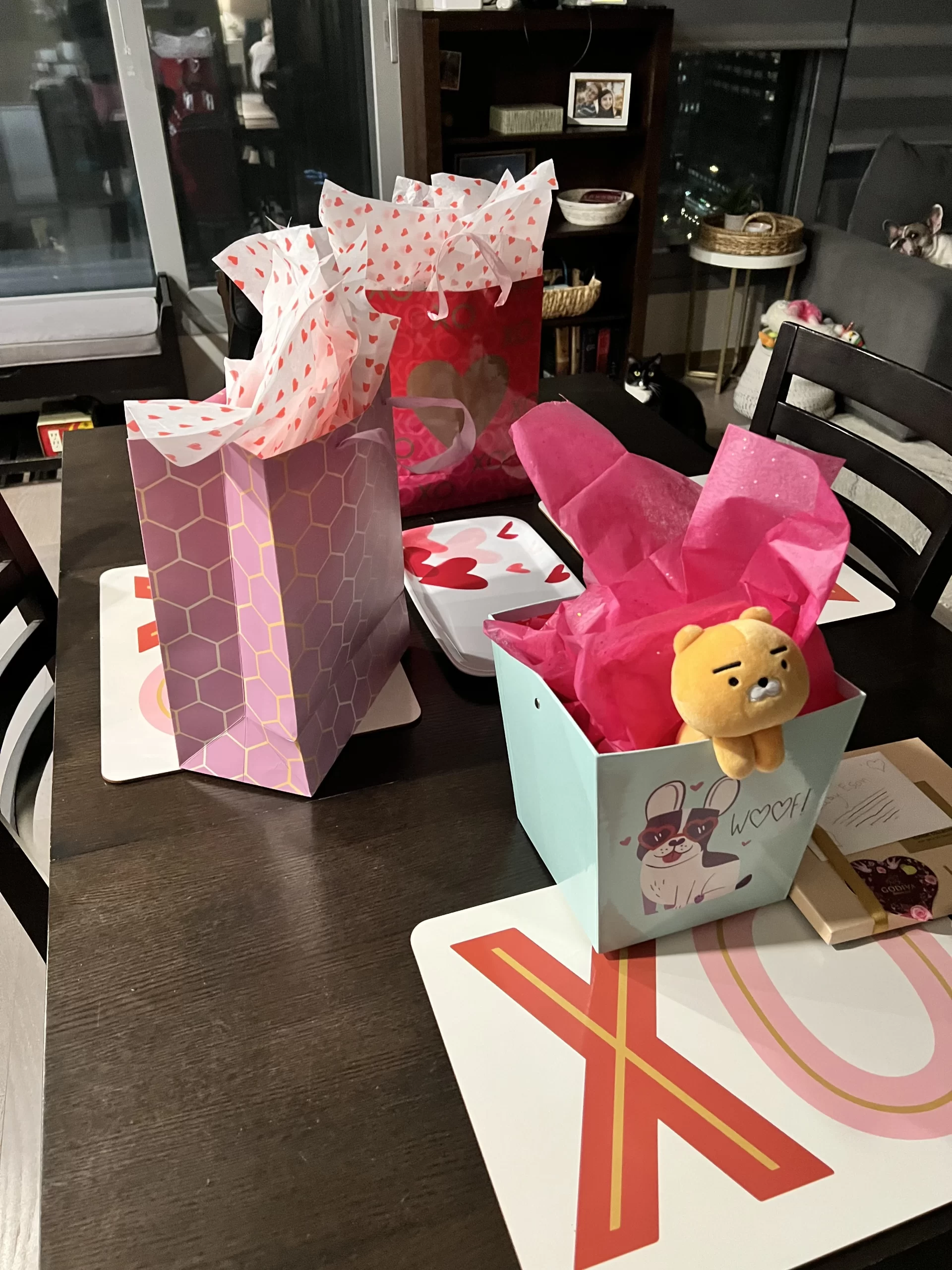 Valentine's Day gifts arranged on a dining table with colorful gift bags, heart-themed wrapping, chocolates, and a plush toy. Giving thoughtful presents is one of the most popular traditions for Valentine's Day in Korea.